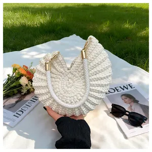 Close-up of a stylish white straw woven conch shaped handbag in an outdoor picnic scene.