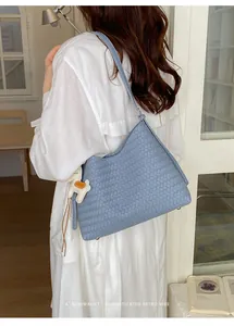 Blaue minimalistische geflochtene Achseltasche von hinten an einem Modell im weißen Kleid.