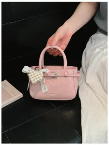 Detail view of a pink textured handbag with pearl heart charm and white lace bow