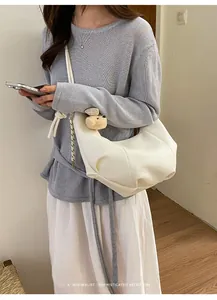 Detailed view of a minimalist cream pleated hobo bag with a cute plush bear charm