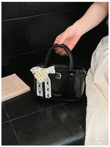Detailed view of chic black glossy bucket bag with pearl heart and lace bow