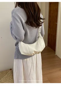 Minimalist white pleated hobo bag shown as an underarm shoulder bag on a model.