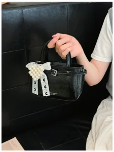 Close-up of a black glossy bucket bag with a pearl heart and lace bow charm.