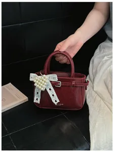 Detail view of a red glossy bucket bag with pearl bow and elegant leather texture.