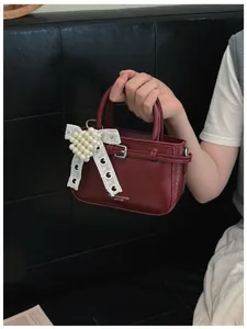 Close-up of a dark red mini handbag with a delicate pearl heart charm and lace bow detail.