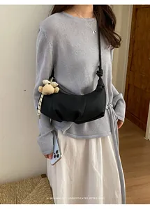 Detailed view of a black pleated crescent shoulder bag with a cute plush bear charm