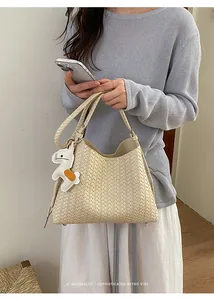 Nahaufnahme einer minimalistischen beigen Webhandtasche mit einem süßen Tieranhänger