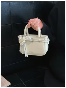 Close-up detail of a minimalist cream leather bucket bag with elegant pearl heart charm