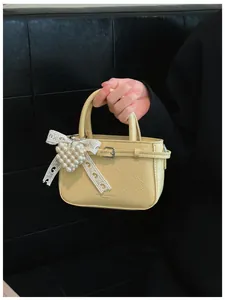 Close-up of a stylish yellow textured handbag featuring a pearl heart and lace bow