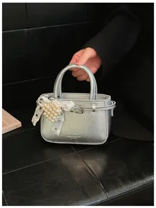 Close-up of a silver tote bag with a unique pearl heart and lace charm detail.