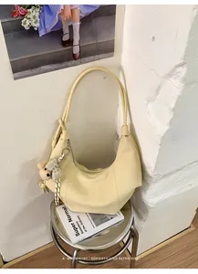 Detail view of a cream yellow pleated retro hobo bag with a cute bear charm on a stool