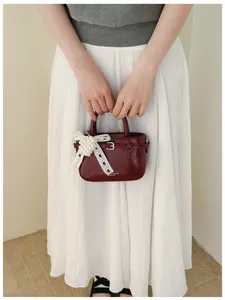 Close-up detail of a burgundy glossy textured handbag with elegant lace bow and pearl charm
