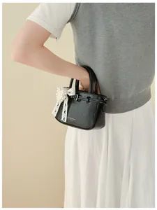 Model holding a glossy black leather bucket bag decorated with a lace pearl bow