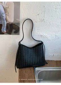 Elegante schwarze geflochtene Unterarmtasche mit minimalistischem Retro-Stil auf Holz