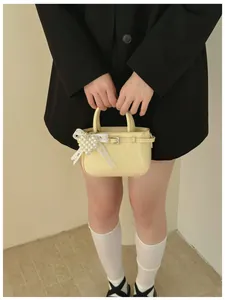 Detail of pale yellow glossy handbag with elegant white lace bow and pearl charm
