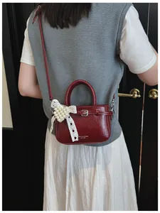 Detailed view of a stylish dark red leather handbag with a decorative pearl lace bow