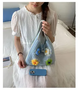 Blue knitted tote bag with colorful 3D flower decorations held by a woman in a white dress