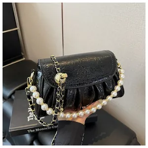 Dettaglio ravvicinato di una borsa in pelle nera a pieghe con elegante tracolla di perle