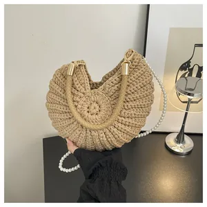 Close-up detail of khaki woven shell handbag featuring pearl strap and golden hardware