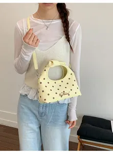 Modella che indossa una mini borsa a tracolla gialla a pois con manico annodato.
