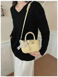 Detailed view of a stylish yellow mini handbag with a pearl bow accessory held by a model.