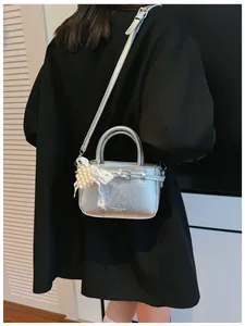 Close-up detail of a silver textured handbag with pearl charm styled on a black coat