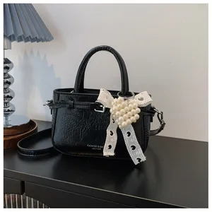 Detail view of textured black leather handbag with elegant pearl heart and lace ribbon charm