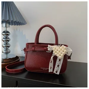 Detail shot of a vintage burgundy wrinkled leather handbag with pearl heart charm.