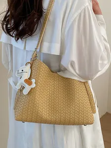 Elegante beige gewebte Schultertasche mit süßem Pferdeanhänger, getragen am Model