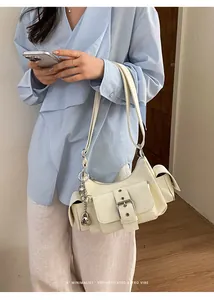 Model wearing a chic cream multi-pocket underarm bag with retro buckle and silver charms.