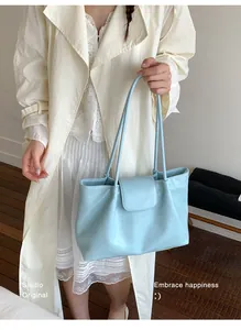 Close-up of a minimalist sky blue pleated tote bag held by a model in a trench coat.