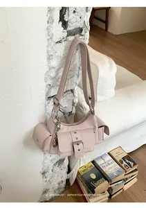 Pink minimalist crossbody bag displayed against a textured white wall with books layout