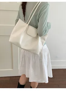 Detail view of a large white minimalist tote bag being worn over the shoulder by a model.