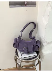 Close-up of a purple suede underarm bag with buckle pocket in a minimalist setting.