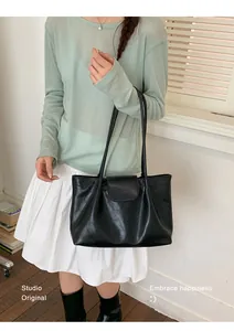Detail view of a minimalist black pleated tote bag styled with a casual outfit on a model.