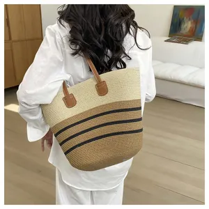 Detail of a handmade straw woven tote bag with stripes worn on a woman's shoulder