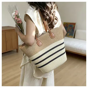 Back view of a woman carrying a stylish woven straw tote bag with black stripes detail