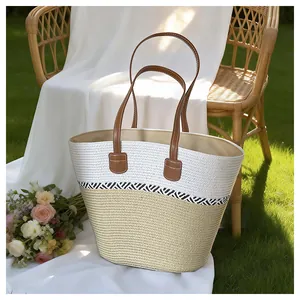 Woven straw beach tote bag with brown leather straps in a scenic outdoor garden setting