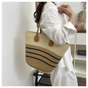 Woven straw tote bag with brown handles and striped pattern carried by a model