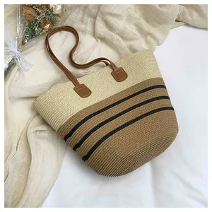 Close-up of a two-tone hand-woven straw tote bag with black stripes and leather handles