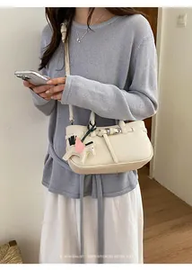 Dettaglio di una borsa a mano color crema minimalista con ciondolo a cavallo.