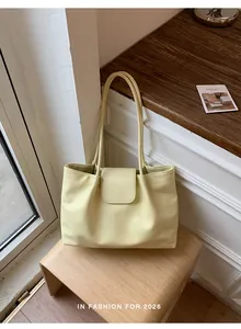 Angled view of a light yellow pleated tote bag placed on a minimalist wooden stool.
