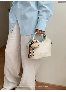 Vue détaillée d'un sac seau crème avec bordure bleu clair et un joli petit pendentif en ours