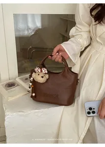 Gros plan d'un sac seau rétro marron avec un charm ours en peluche et logo embossé.
