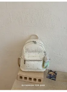 Detalle de mochila blanca con estrellas, bordado y colgante de conejo peluche