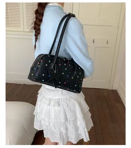 Vista detallada de un bolso de hombro negro con patrones de estrellas de colores.