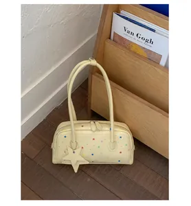 Detalle del bolso de hombro amarillo pálido con estrellas y colgante.