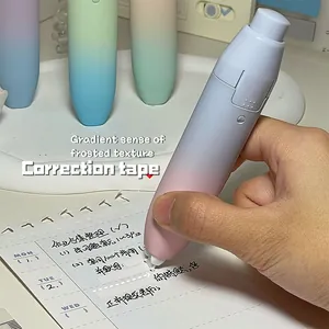 Close-up of a hand using a gradient macaron retractable correction tape on a notebook