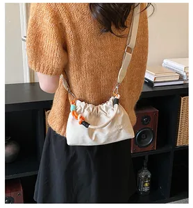 Détail d'un mini sac à bandoulière en nylon crème avec une poignée en corde colorée.