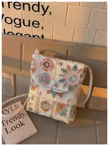 Dettaglio del ricamo floreale su una borsa a tracolla etnica color crema per cellulare